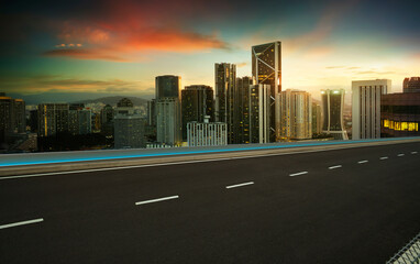 Empty asphalt road with modern city skyline at sunset