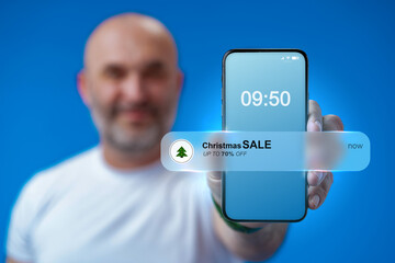 Smartphone shows Christmas sale notification at 09:50 with man smiling in background