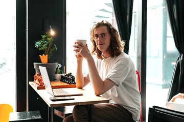 Young man enjoys coffee while working on laptop in a cozy cafe setting