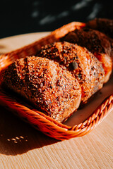 Freshly baked bread rolls in a woven basket on a wooden table during morning light