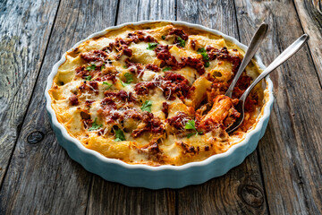 Bolognese pasta casserole - baked rigatoni noodles with bolognese sauce, mozzarella cheese and béchamel sauce on wooden table