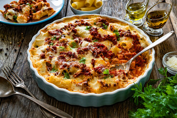 Bolognese pasta casserole - baked rigatoni noodles with bolognese sauce, mozzarella cheese and béchamel sauce on wooden table