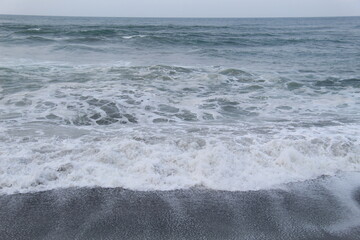 Ocean waves rolling onto the shore with white foam under an overcast sky. Ideal for seascape, coastal, nature, or tranquility-themed visual content