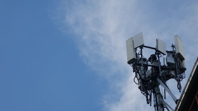 Cellular telecommunications tower with antennas and equipment against blue sky with white clouds and power lines