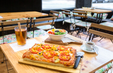 Restaurant table with vegetarian focaccia, colorful salmon and edamame poke bowl, iced tea and espresso on wood, inviting casual lunch with fresh choices. Organic and natural fast food concept