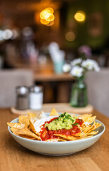 Nachos with tortilla chips, salsa, sour cream, and guacamole served on a table at a restaurant.