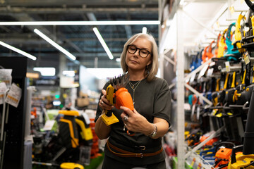 Woman examines gardening tools in a hardware store while shopping for home improvement supplies