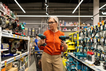 Woman shopping for power tools in a hardware store while carrying two drills