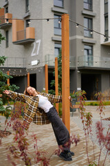 young woman in casual outfit stretches playfully against post in urban park setting. relaxed pose...