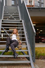 casual fashion woman sitting stairs outdoors, relaxed urban lifestyle. young woman in plaid shirt...