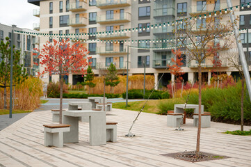 modern urban park with concrete tables and benches under string lights, surrounded by vibrant...