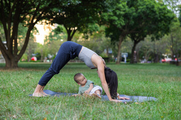 oung woman performing yoga with baby son outdoors park