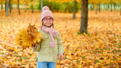autumn child holding leaves in park. girl in warm clothing surrounded by vibrant fall foliage...