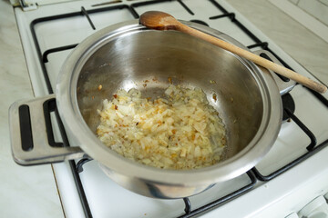 Preparing onion base for pumpkin soup in stainless steel pot on gas burner.