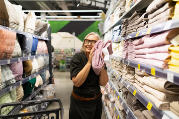 Smiling woman enjoying shopping for blankets in a cozy home goods store aisle filled with soft textiles