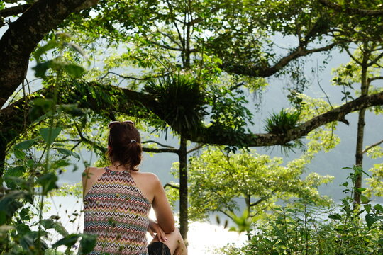 A woman enjoying a scenic view in a lush green tree branches frame view of a tranquil lake with floating structures set against a misty mountain backdrop close to the Begnas Lake in Pokhara in Nepal