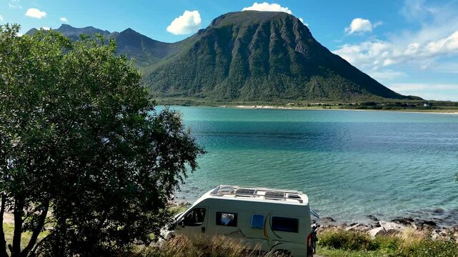 A camper van parks near a tranquil fjord in Norway, surrounded by stunning mountains and lush greenery. The scene captures a sense of adventure and relaxation in natures beauty.