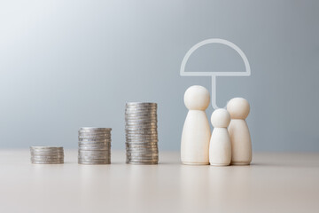Wooden figures representing a family beside stacked coins under an umbrella symbol, illustrating...