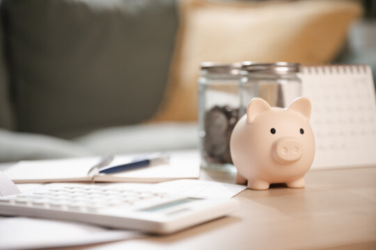 A pink piggy bank on a wooden desk with coins, calculator, and notebook, symbolizing savings planning, financial management, and budget organization for monthly money goals.