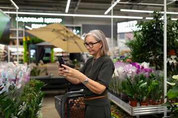 Woman shopping for plants while using a smartphone in a garden center during day time