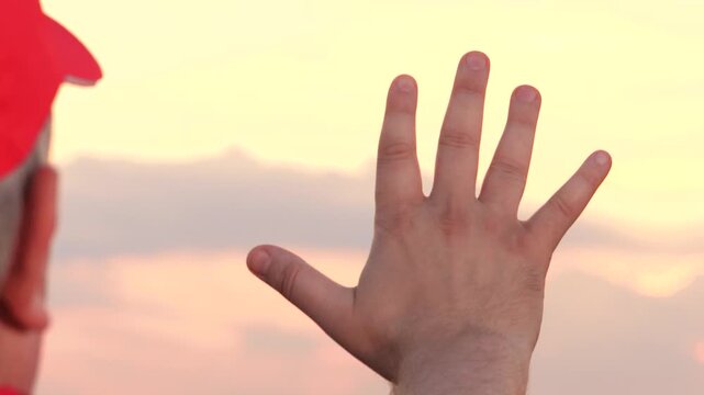 Male farmer showing hand at sunset sky dry wheat harvest back view closeup. Man agronomist agricultural worker goodbye bye sun at evening cloudscape countryside meadow plantation natural landscape