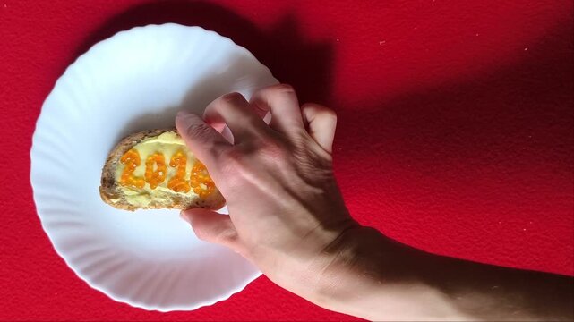 sandwich with butter and red caviar. The numbers 2026. A white plate on a red background. Dill sprigs. 2026 made of caviar on a sandwich. A woman's hand moves the plate.