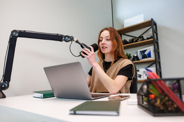 A young woman talks into a cardioid mic on a boom arm at a white desk in a compact studio. A laptop, notebook, and phone sit nearby as soft light gives shallow depth. © True Pixel Art