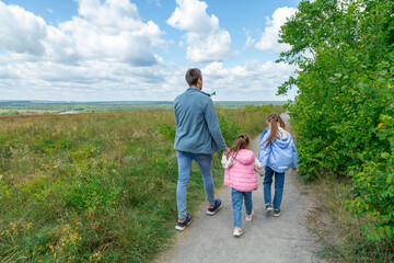 Father and daughters walking in a field on a sunny day