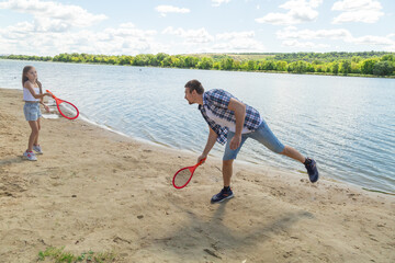 Father and daughter having fun on the beach during summer vacation playing beach tennis