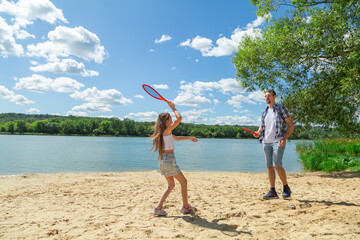 Father and daughter having fun on the beach during summer vacation playing beach tennis