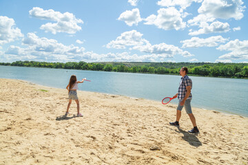 Father and daughter having fun on the beach during summer vacation playing beach tennis