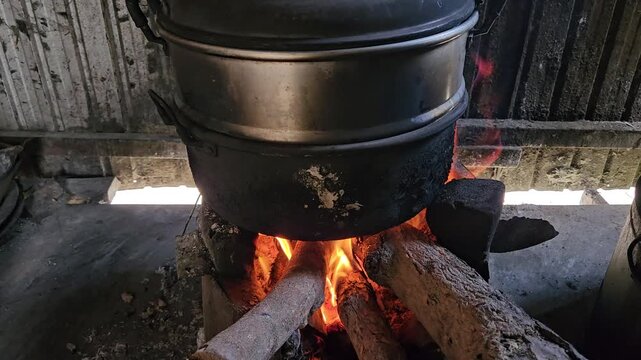 A close-up of intense wood logs burning fiercely beneath a soot-stained metal cooking pot, traditional method of steaming Vietnamese cakes.
