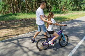 Obraz premium Child trying the bicycle. Happy father with daughter are having fun in forest at summertime.