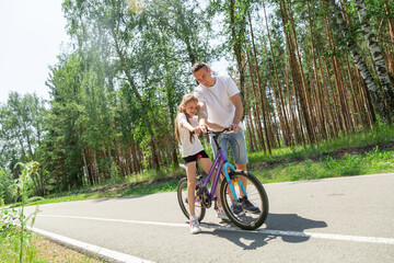 Obraz premium Father teaching his daughter how to ride a bicycle in forest