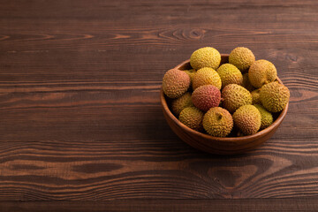 Ripe Lychee on clay bowl on brown wooden, side view, copy space, minimalism