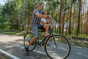 Obraz premium Young father with his little daughter on bicycle in summer sunny forest