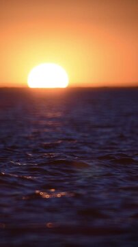 large sun sets over the horizon, in the foreground, the dark blue waves of a large lake,