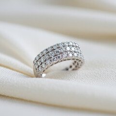 Close up shot of a silver ring with multiple rows of diamonds on a white fabric surface