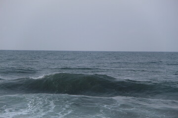 Ocean waves crashing on the shore under a cloudy sky. Blue sea water with white foam shows the power and beauty of nature, perfect for themes of travel, nature, energy, and environment
