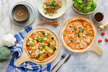 Two pizzas with various side dishes arranged on a table, creating a delightful culinary spread. The vibrant pizzas with fresh toppings are complemented by other plates of food