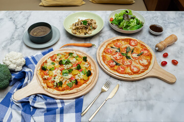 Delicious pizzas and a variety of healthy foods artfully arranged on a table setting. Displaying a diverse selection of culinary delights ready to be enjoyed