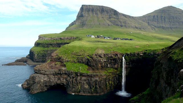 Experience the breathtaking beauty of Mulafossur Waterfall as it tumbles into the ocean, set against the stunning backdrop of Gasadalur village in the Faroe Islands during a clear day.
