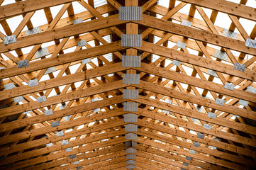 Symmetrical view of wooden roof trusses with metal plates in a modern building under construction. Abstract architectural pattern with repeating wooden beams and geometric structure.