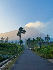 village road with view of active volcano emitting smoke in the morning