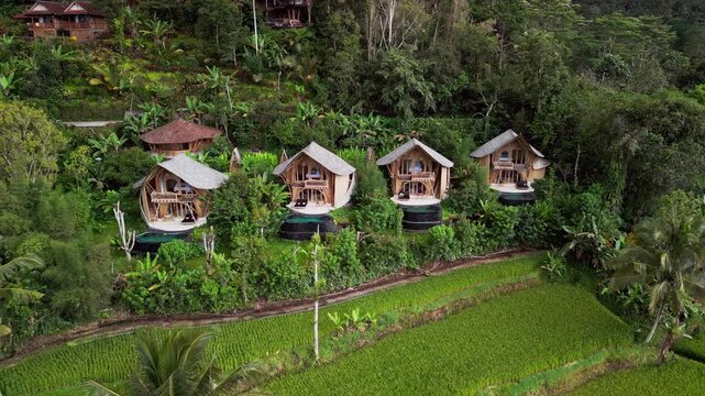 Drone footage of Sidemen Bali featuring bamboo accommodation with infinity pools built above rice fields, tropical vegetation, and rugged hills, offering a clear view of rural island hospitality