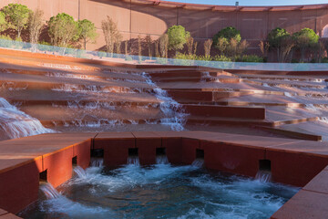 Water amphitheater or canyon in Krasnodar's city park or Galitsky Park. Architectural landscape with cascading red terraces over which water flows. Plants grow along curved red wall. Fall 2025..