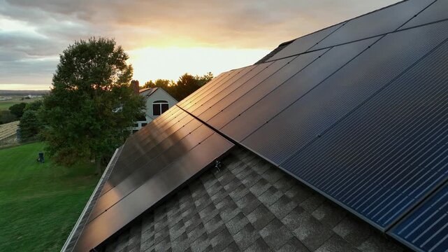 Drone close up showing solar panel on rooftop of american houses during cloudy sunset. Aerial flyover shot. Green grass in backyard. Production of green eco friendly energy at home.
