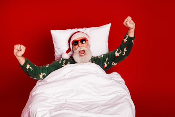 Santa in green pajama celebrates in bed with red backdrop creating a cozy Christmas home scene