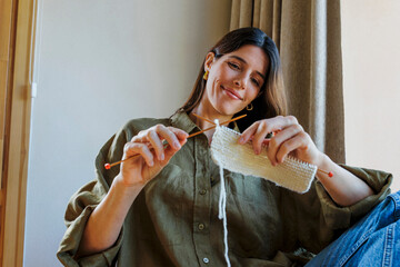 Woman knitting with wool indoors, smiling and focused on her craft
