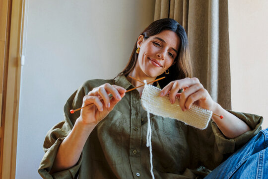 Woman knitting with wool indoors, smiling and focused on her craft